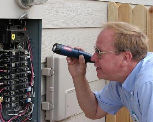 man in blue shirt inspecting a circuit breaker